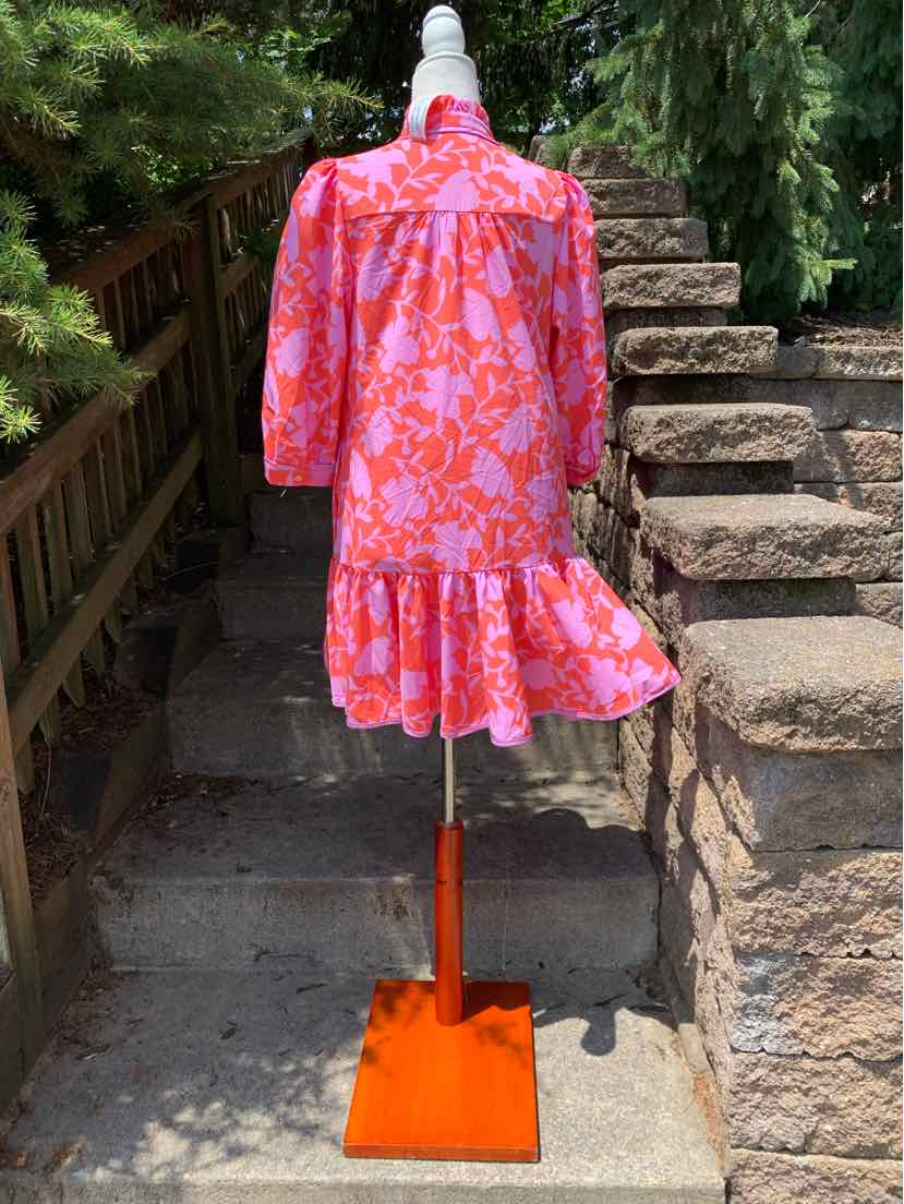 Pink floral patterned knee-length dress with long puff sleeves and a ruffled hem on a mannequin outdoors.