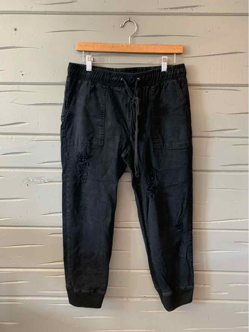Black large solid pants with an elastic waistband and drawstring, displayed hanging against a wooden background.