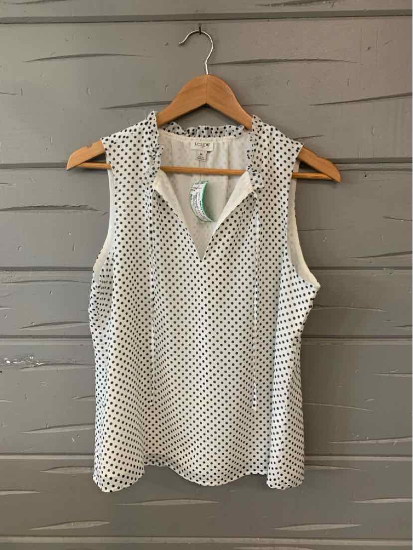 White sleeveless blouse with black polka dots, V-neck, and lightweight fabric on wooden hanger.