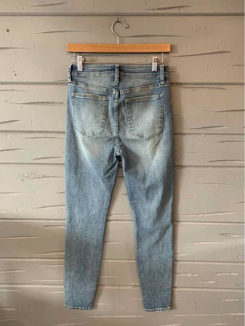 Light blue slim-fit denim jeans with faded wash and back pockets hanging on a wooden hanger against a beige wall.
