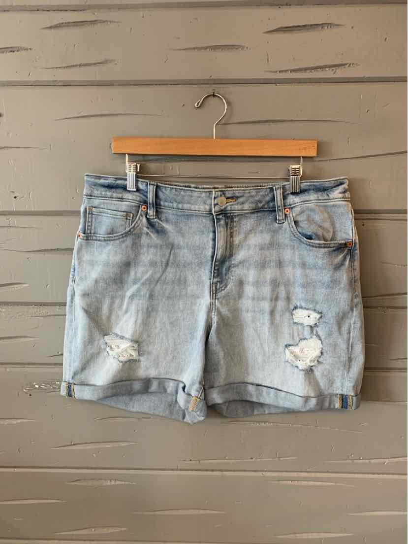 Light wash denim shorts with distressed patches and rolled hems hanging on wooden hanger.