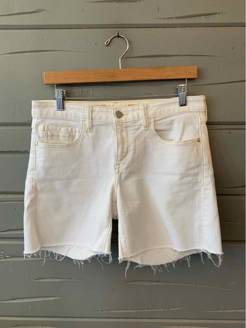White denim shorts with frayed hems, front pockets, belt loops, and a button closure hanging on a wooden hanger.