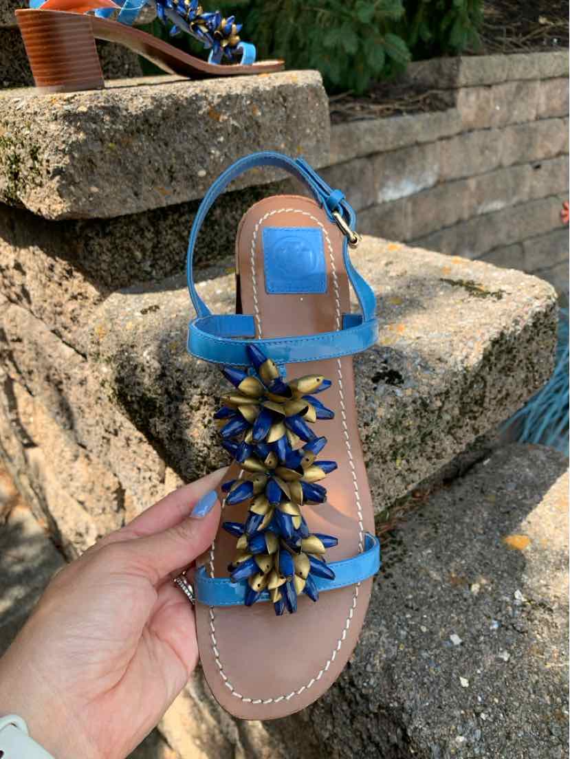 Blue leather flat sandal with ankle strap and decorative gold and blue leaf embellishments on the front.