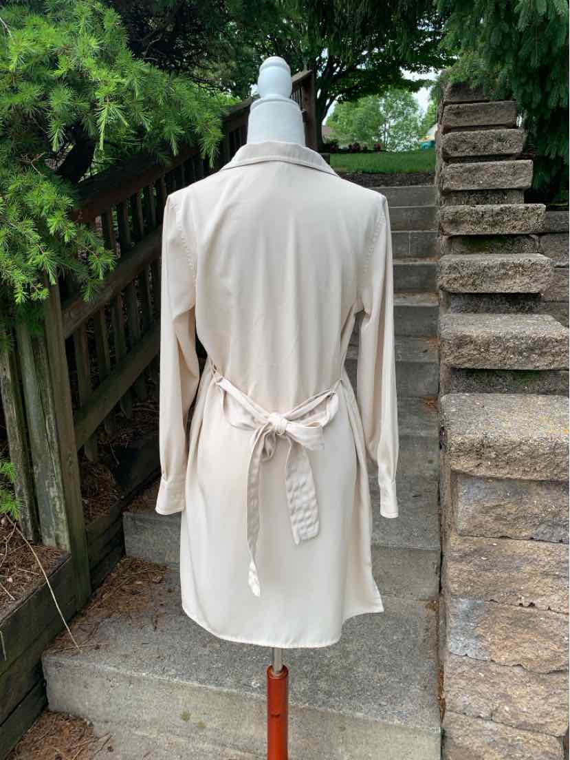 Light beige long-sleeve trench coat with a belted waist and classic collar, hanging outdoors.