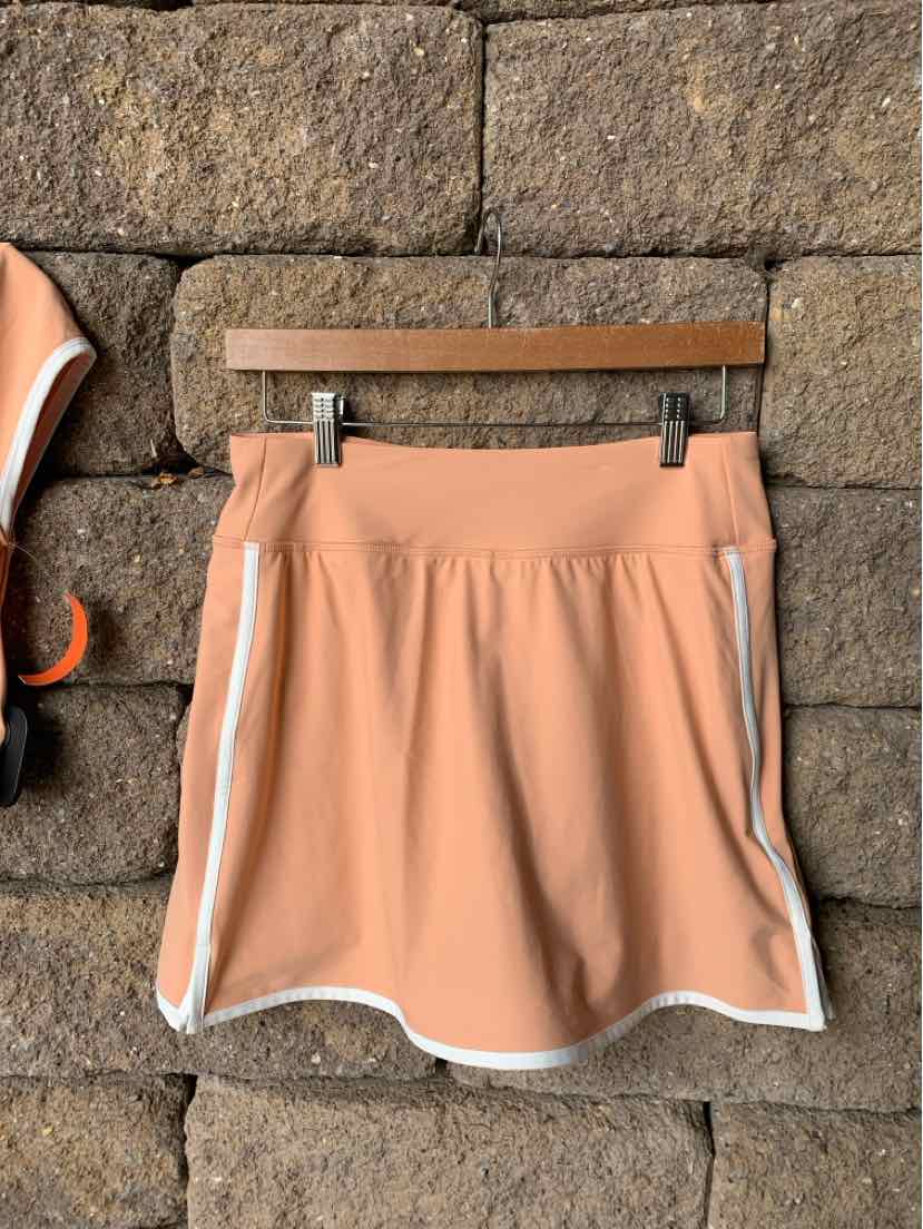 Light peach athletic skirt with white trim and side pockets, made from smooth performance fabric.