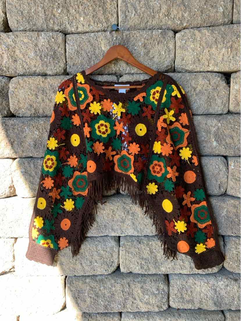 Black cropped cardigan with a colorful floral pattern, long sleeves, and an open front, displayed on a hanger.