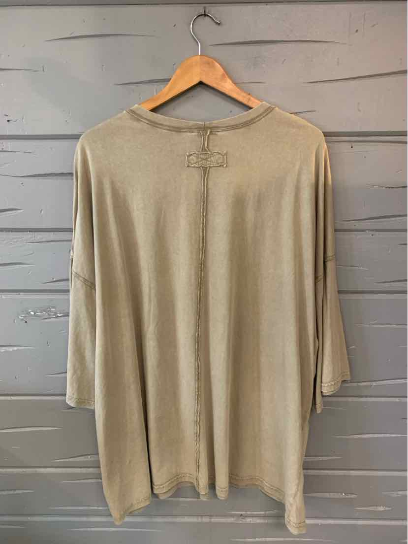 Beige loose-fit long-sleeve tunic with a rounded neckline and subtle stitched chest detail, hanging on a wooden hanger.