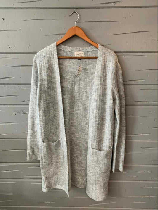 Light gray open-front knit cardigan with long sleeves and front pockets hanging on wooden hanger.