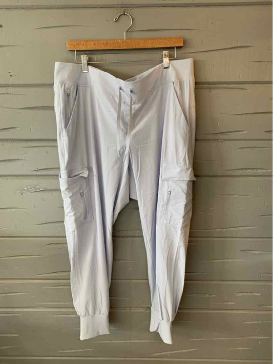 Light gray tapered jogger pants with elastic cuffs and side seams hanging on wooden hanger against wooden wall.