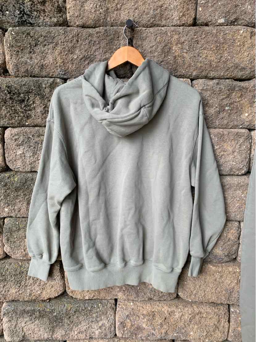 Light gray Nike hoodie with long sleeves, ribbed cuffs and hem, displayed from the back on a wooden hanger against a stone.