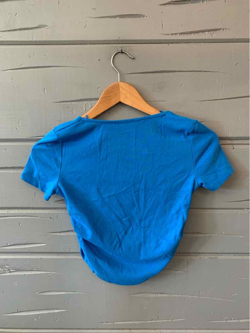 Bright blue short-sleeve fitted top with round neckline on wooden hanger against gray wooden wall.