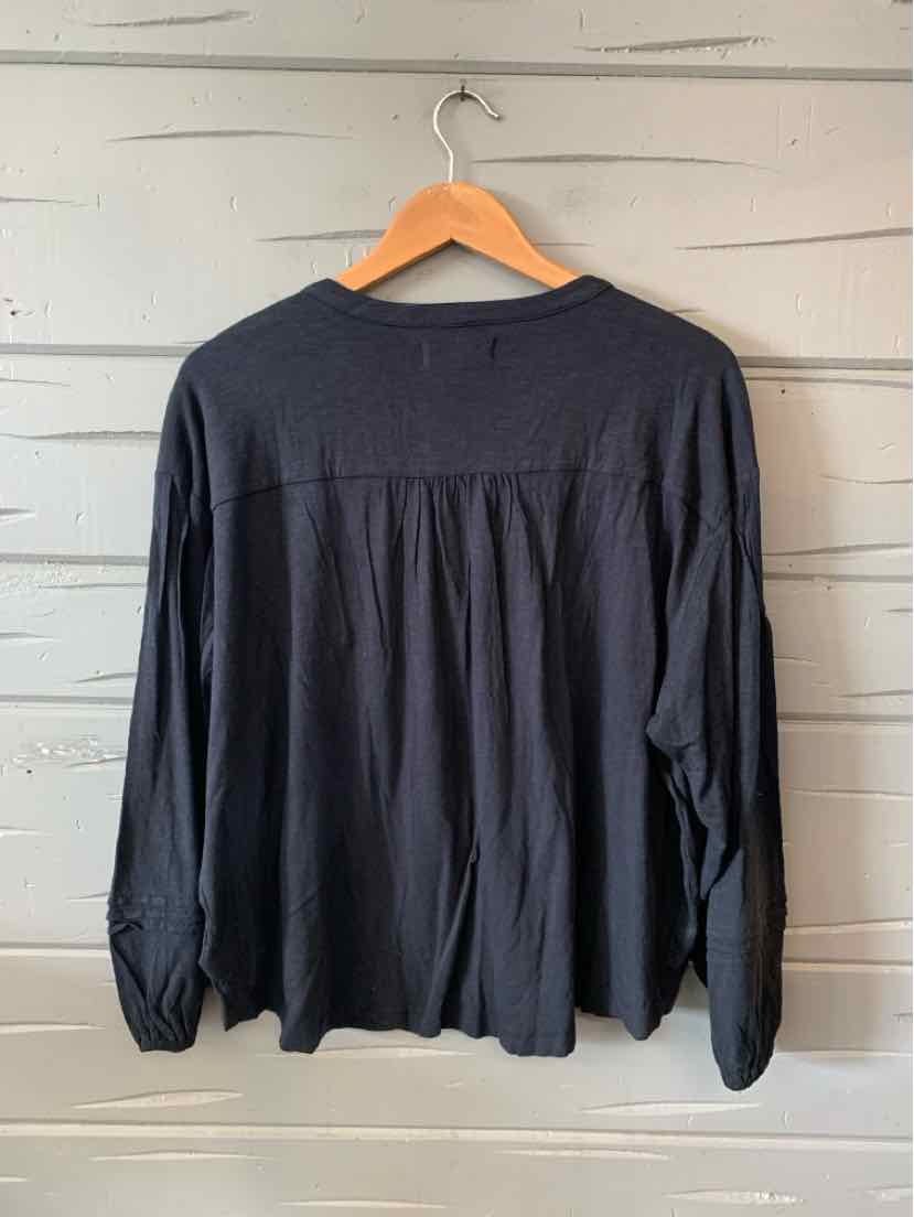 Black long-sleeve blouse with loose fit and subtle pleats at the back, hanging on wooden hanger.