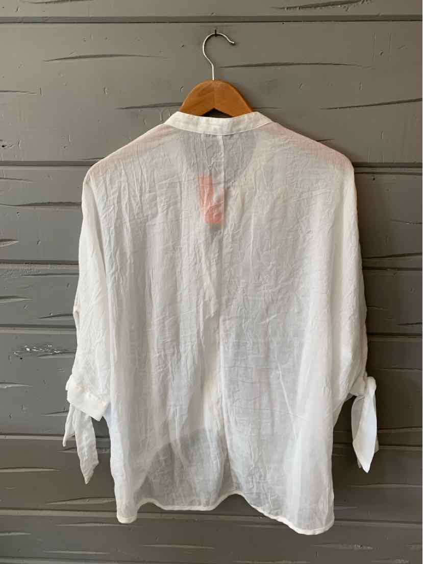 White long-sleeve blouse with lightweight fabric and tied cuffs hanging on wooden hanger.