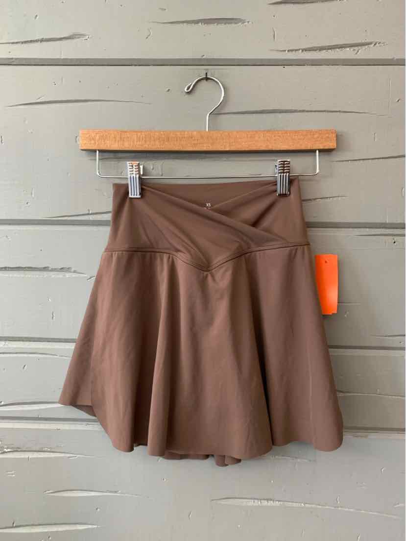 Brown A-line mini skirt with a wide waistband and front pleats on a wooden hanger.