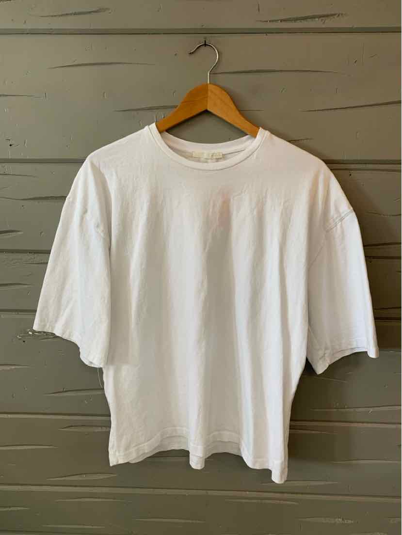 White short-sleeve oversized cotton T-shirt with crew neckline hanging on wooden hanger.