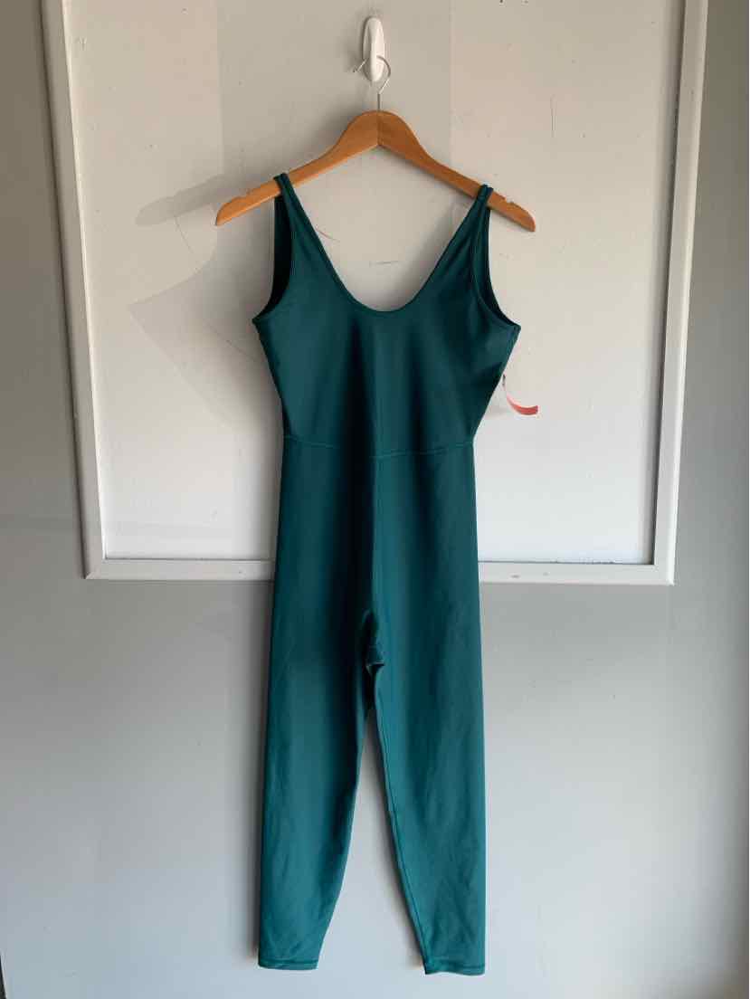 Teal sleeveless jumpsuit with fitted waist and tapered legs hanging on wooden hanger against white wall.