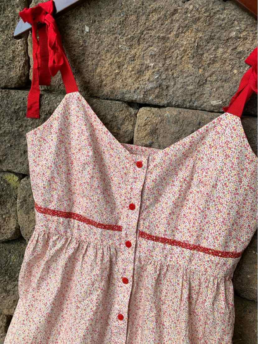 Floral print sleeveless dress with red button front and red ribbon tie straps.