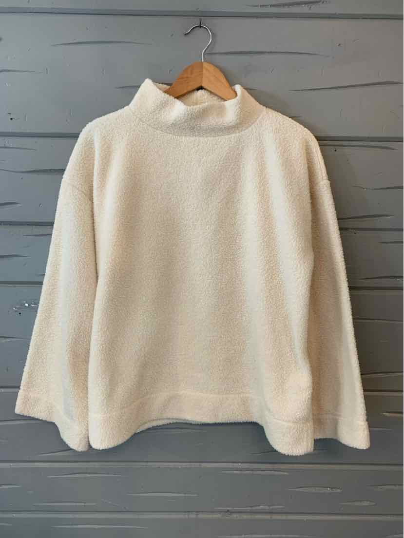Cream-colored sherpa pullover with a loose fit and high collar hanging on wooden hanger.