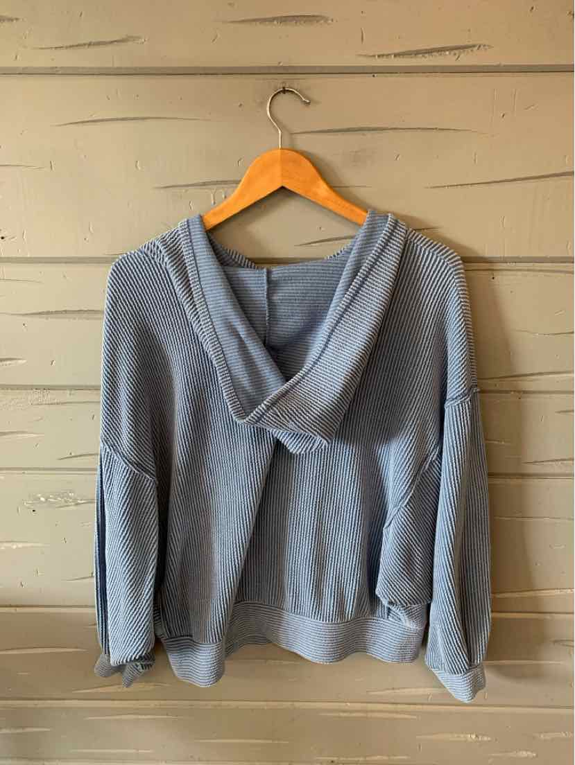 Soft blue medium hoodie with relaxed fit and wide hood on wooden hanger against beige wall.