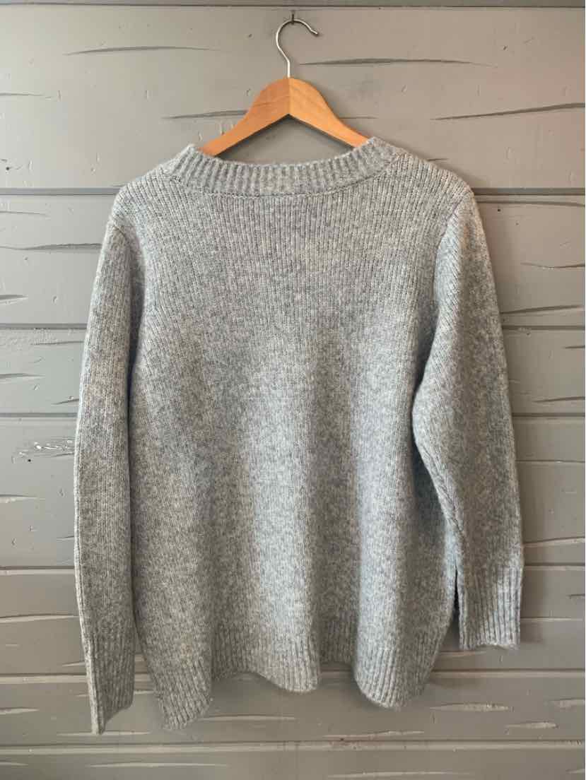 Light gray knit sweater with long sleeves and ribbed crew neckline hanging on wooden hanger.
