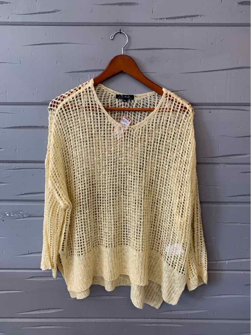 Light yellow oversized knit sweater with open-weave pattern and long sleeves on wooden hanger.