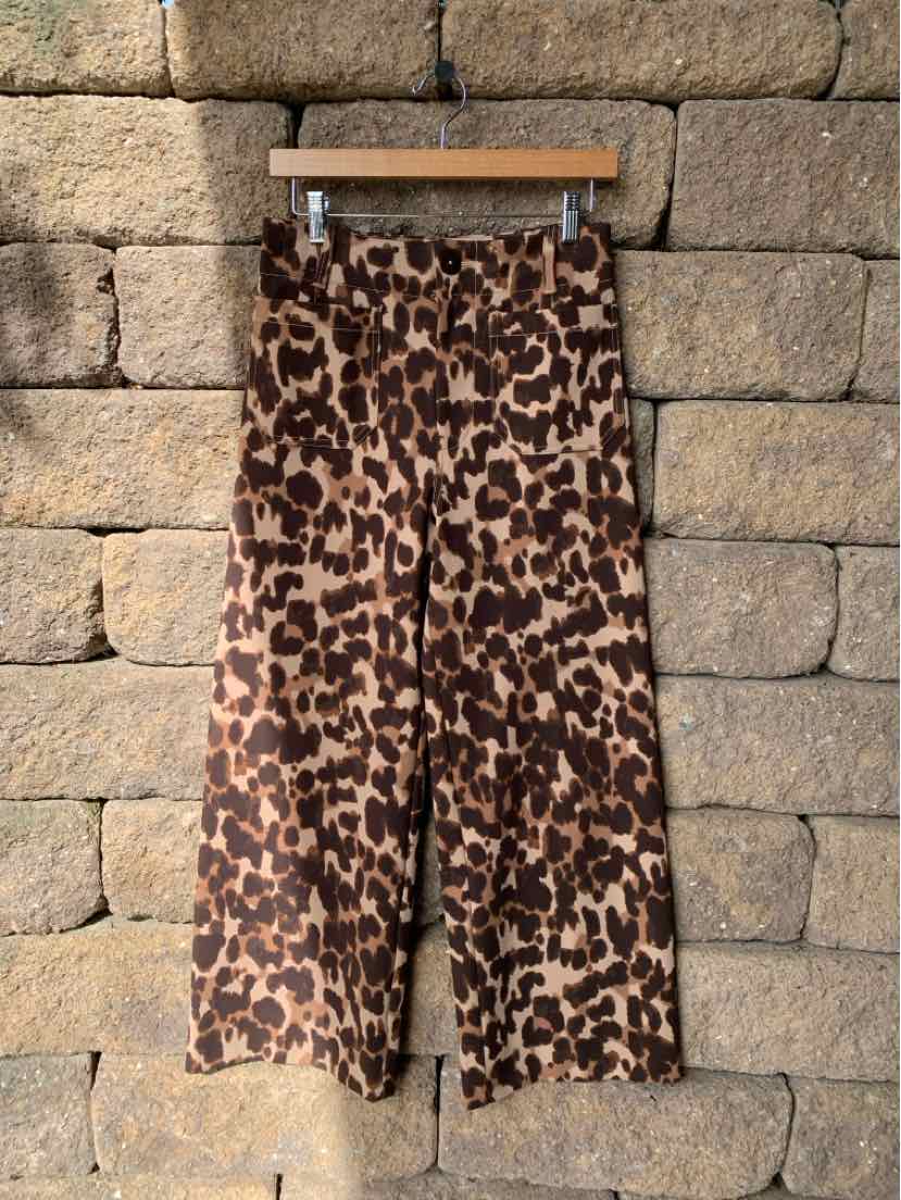 Brown and black cheetah-print wide-leg trousers hanging against a stone wall.