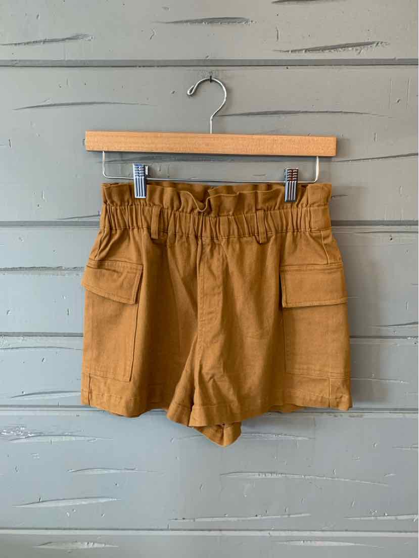 Tan high-waisted shorts with elastic paperbag waist and front flap pockets hanging on wooden hanger.