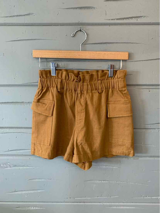 Tan high-waisted shorts with elastic paperbag waist and front flap pockets hanging on wooden hanger.