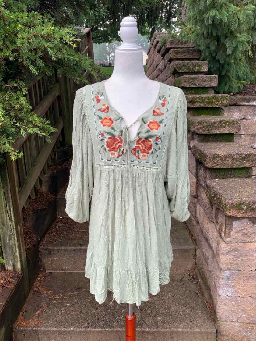 Light green flowy tunic dress with floral embroidery on the chest, V-neck, and three-quarter sleeves.