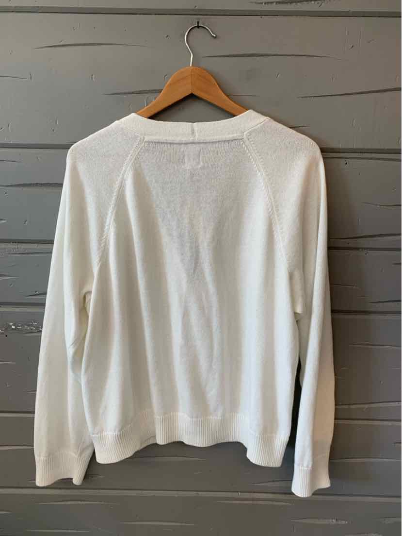 White long-sleeve sweater with crew neck and ribbed cuffs hanging on wooden hanger.