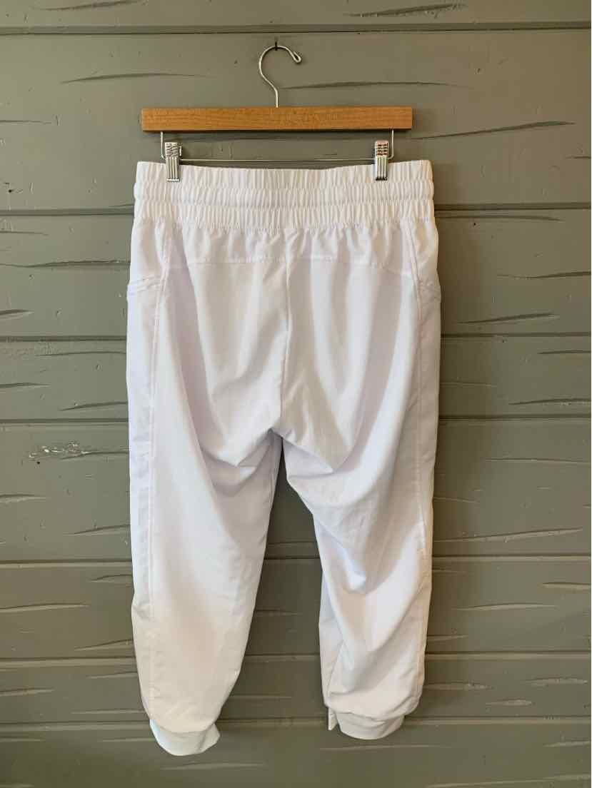 White cropped athletic pants with elastic waistband and rolled cuffs hanging on wooden hanger.