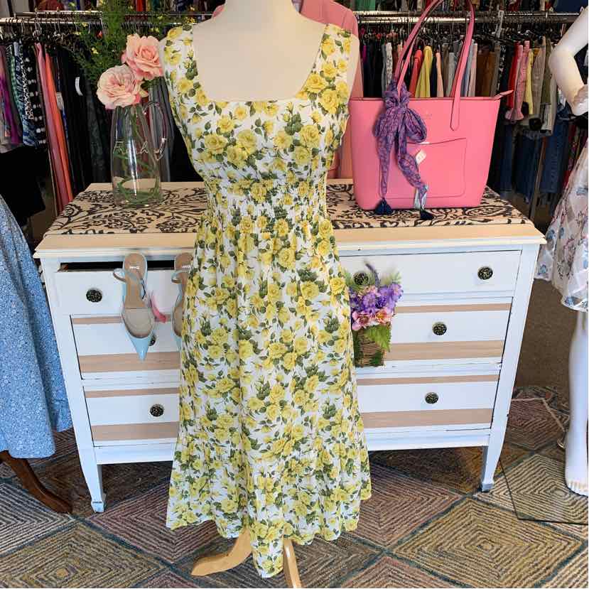 Yellow floral sleeveless dress with cinched waist and square neckline on mannequin.
