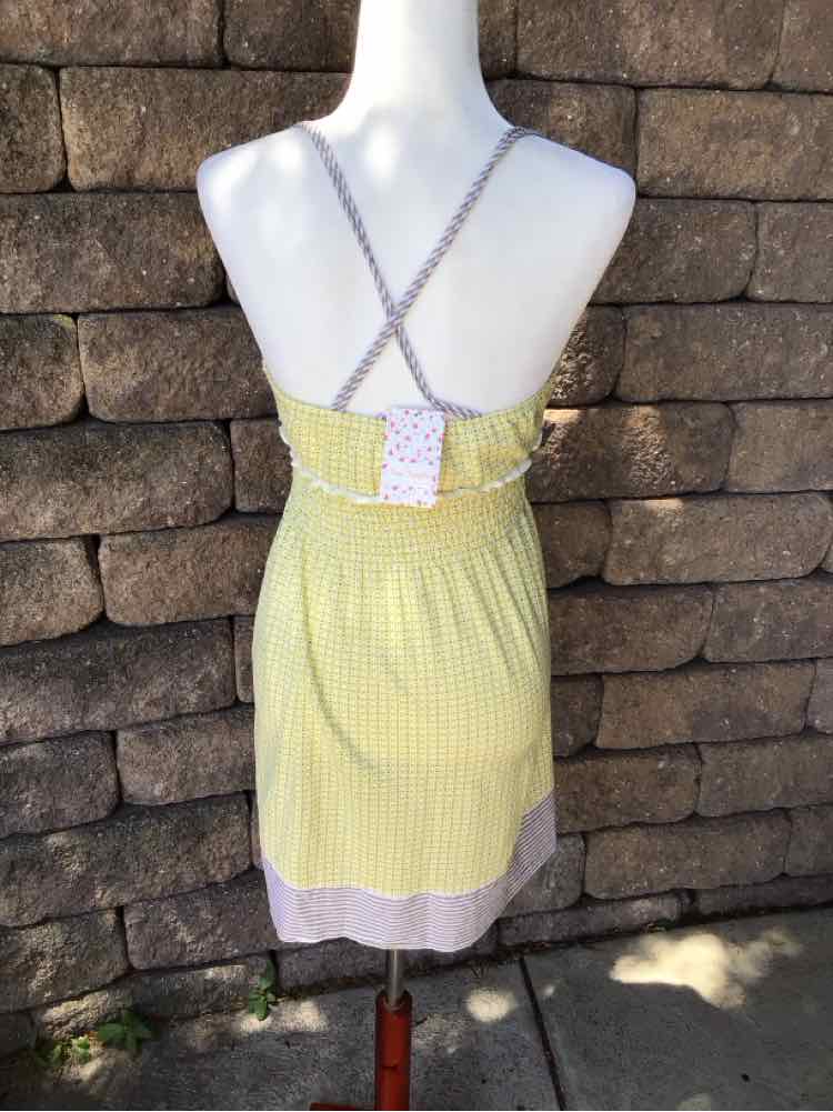 Light yellow sundress with thin crisscross straps and white trim at hem, fitted waist with gathered fabric.