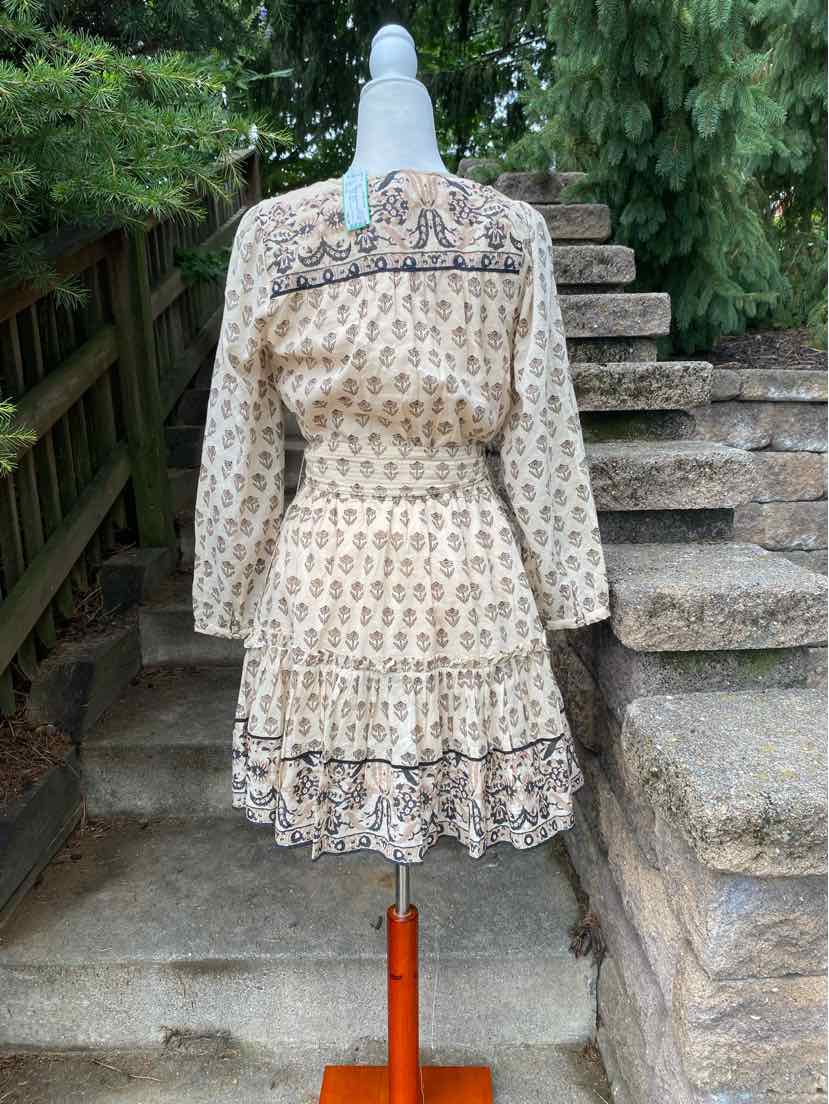 Cream floral long-sleeve dress with a cinched waist and tiered skirt on a white mannequin outdoors.