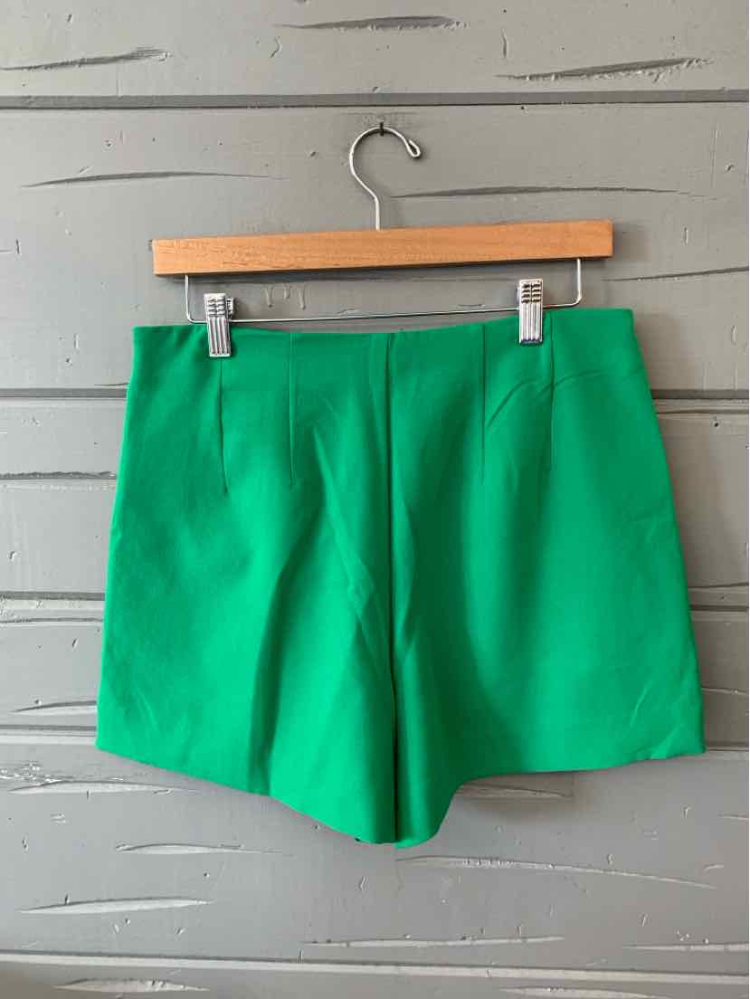 Bright green high-waist tailored shorts with front pleats and a smooth finish hanging on wooden hanger.