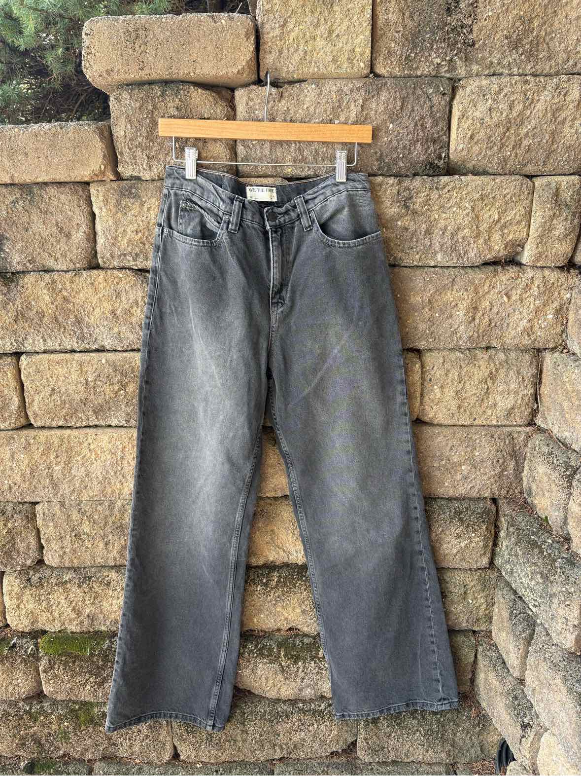 Black washed denim jeans with a straight-leg fit, belt loops, front pockets, and a button closure, hanging from a wooden.