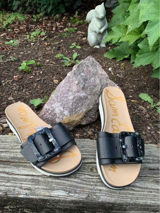 Black slide sandals with wide straps and large buckles, tan footbeds, size 6.