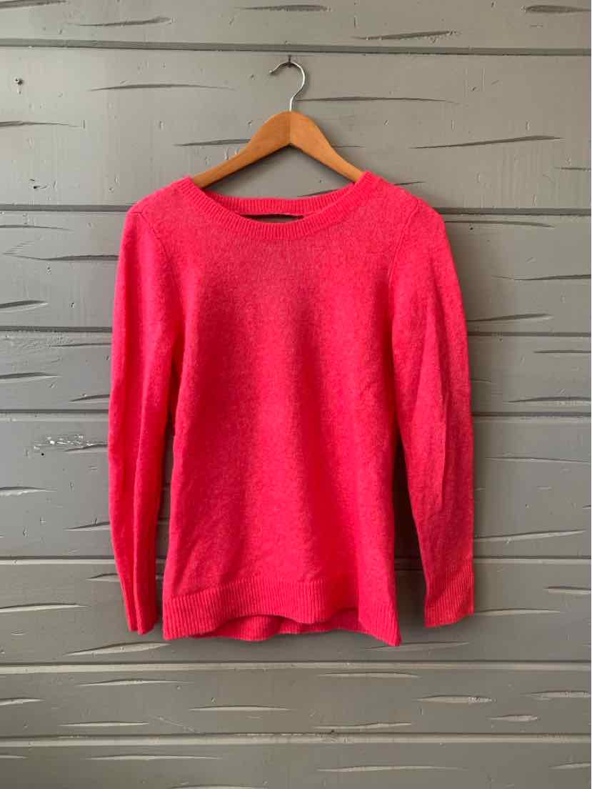 Bright pink long-sleeve knitted sweater with crew neckline on wooden hanger against gray wooden background.