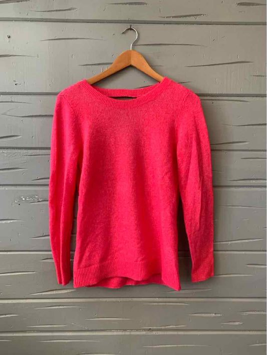Bright pink long-sleeve knitted sweater with crew neckline on wooden hanger against gray wooden background.