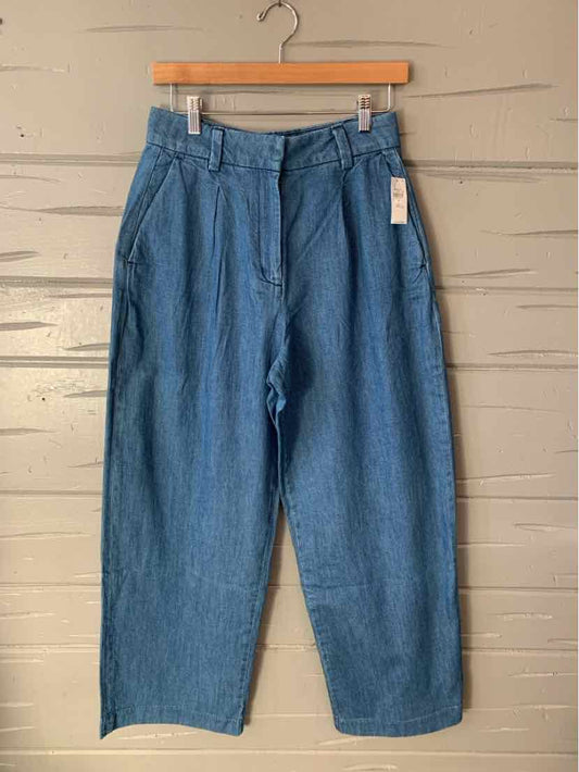 High-waist blue denim trousers with pleats and wide legs, size 4, hanging on wooden hanger.