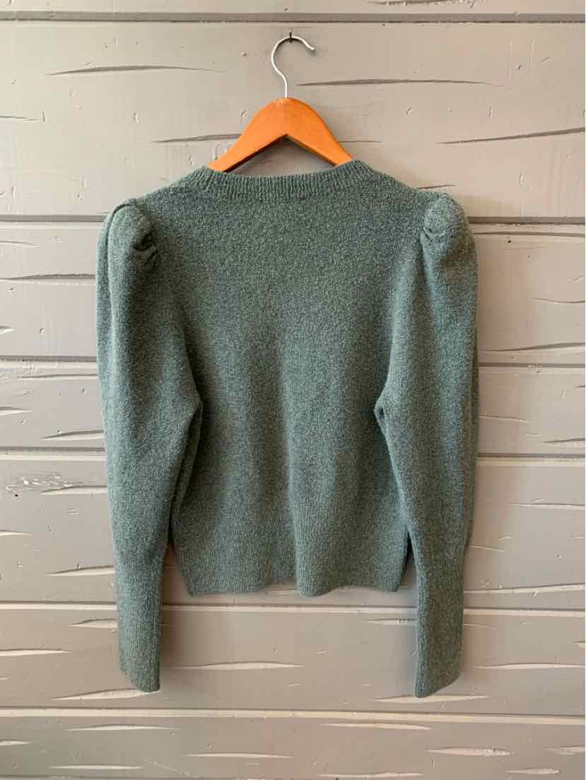 Green knit sweater with puffed shoulders and long sleeves hanging on wooden hanger.