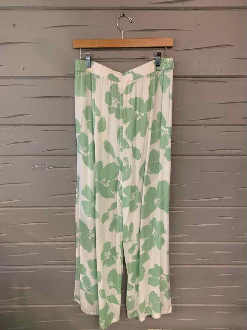 White wide-leg pants with oversized green floral print and a high waist hanging on wooden hanger.