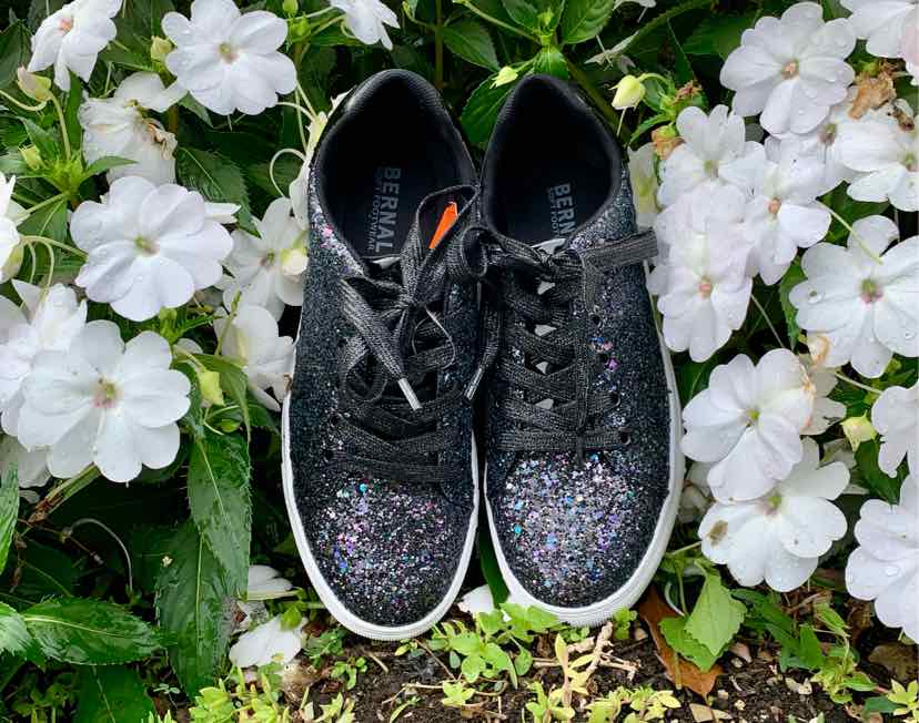 Black low-top sneakers with sparkling glitter on the toe and sides, white soles, and black laces.