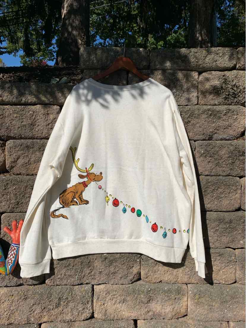 White long-sleeve holiday T-shirt featuring the Grinch and a colorful string of ornaments across the back.