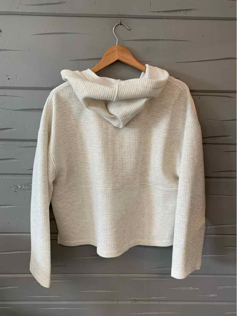Light gray hooded sweatshirt with long sleeves and a relaxed fit, hanging on a wooden hanger against a gray wooden wall.