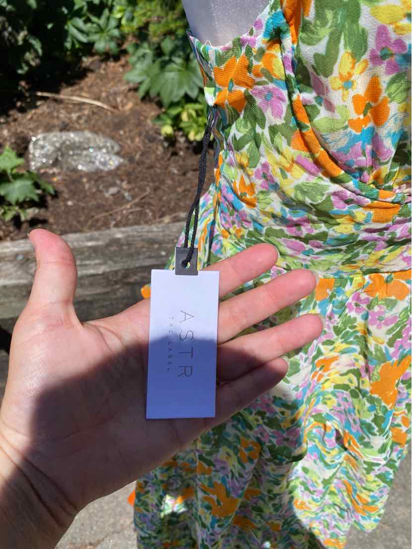 Colorful floral dress in green, orange, purple, and white with a tag attached, worn by a person outdoors.