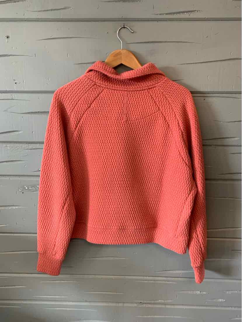 Coral knit sweater with textured pattern, long sleeves, and folded collar on wooden hanger.