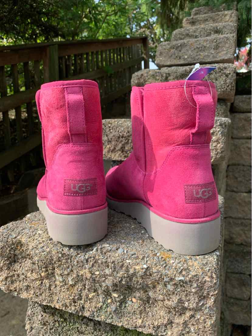 Bright pink suede UGG boots with rounded toes, stitched panels, logo patches, and thick light gray soles.