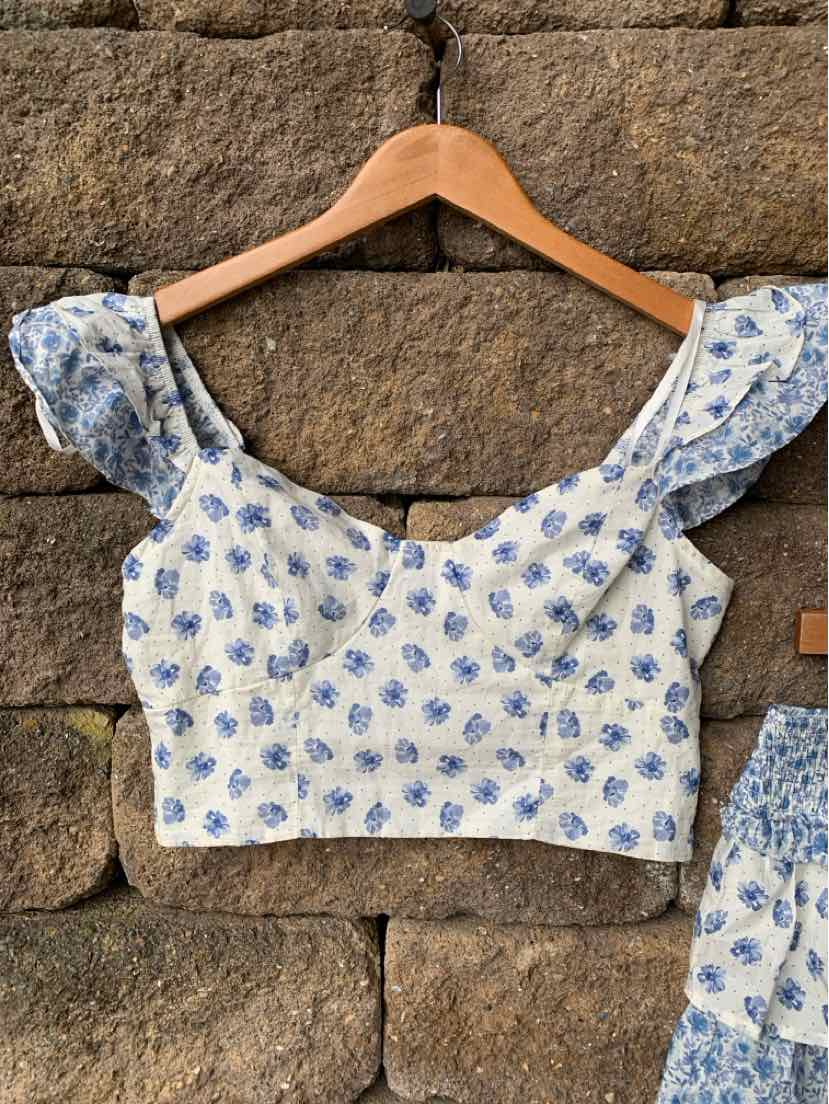 White crop top with blue paisley print and ruffled shoulder straps on wooden hanger.