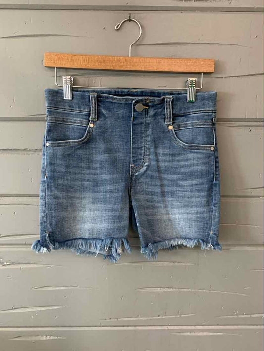 Blue denim women's shorts with frayed hems and front pockets hanging on wooden hanger.